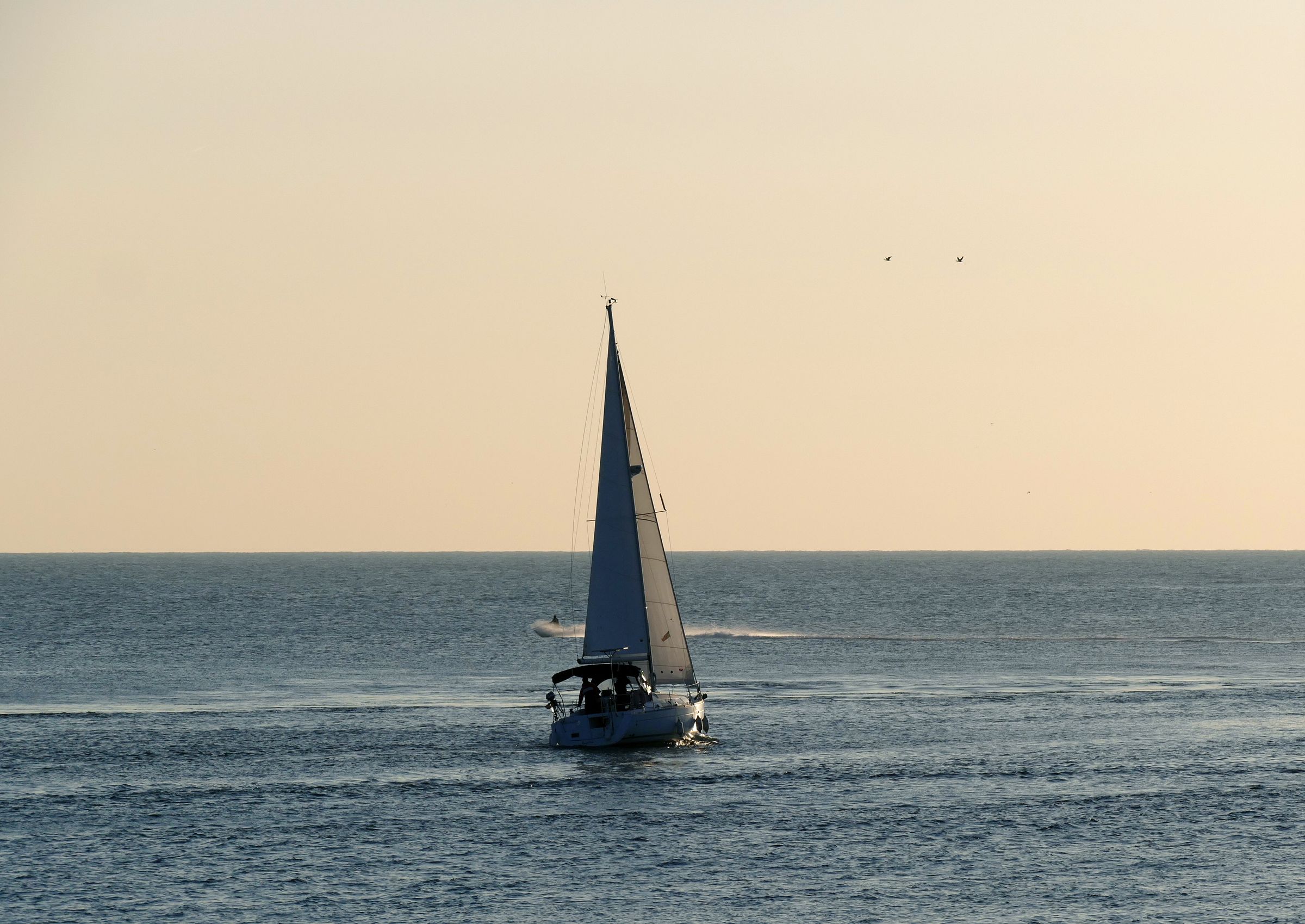 A sailboat moving across a calm sea at dusk